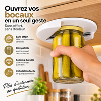 Main insérant un bocal de cornichons dans l'ouvre-bocaux blanc CalmaOuvre fixé sous un meuble de cuisine, pour ouvrir le couvercle sans effort