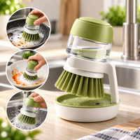 Brosse à vaisselle verte et blanche CalmaBrosse posée sur son support avec réservoir de savon rempli, entourée de trois usages : poêle, assiette et rinçage