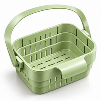 Panier égouttoir vert avec anse, poignée rabattable et parois ajourées, vu en angle sur fond blanc.